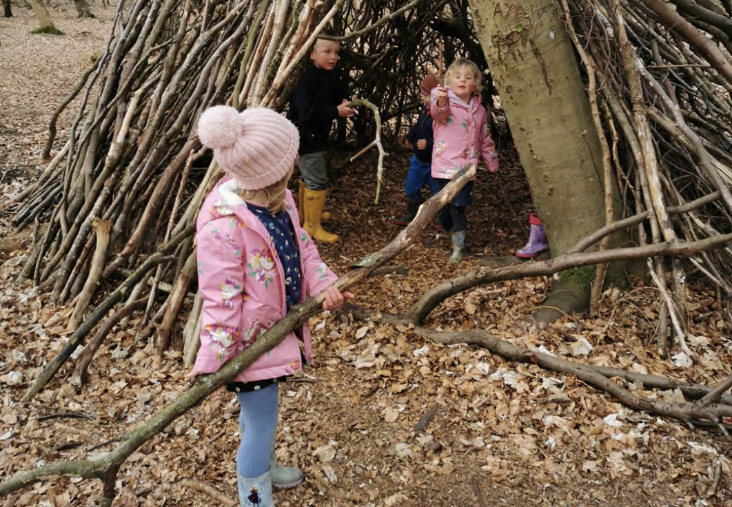 Children in the woods building a den out of fallen branches.