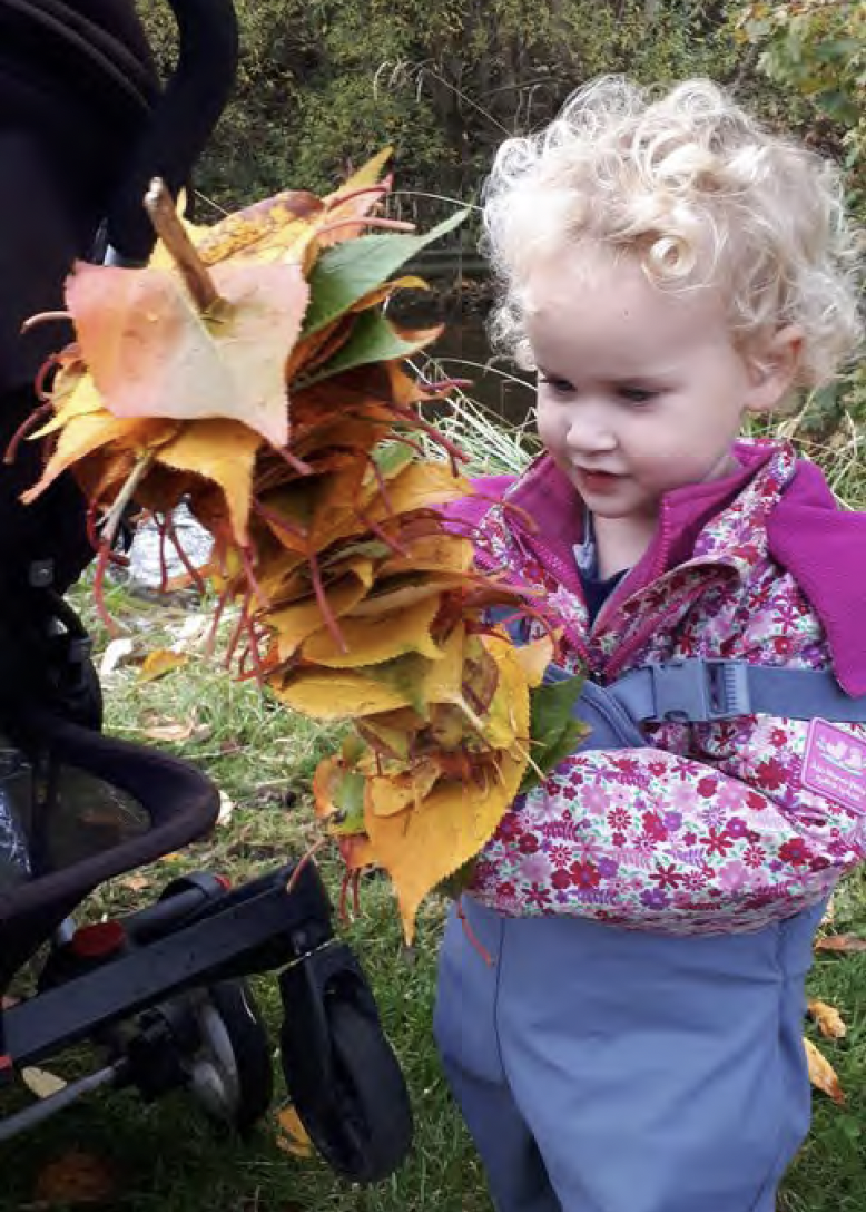 Young child with a leaf kebab which is a fallen stick with colourful fallen leaves skewered onto it.