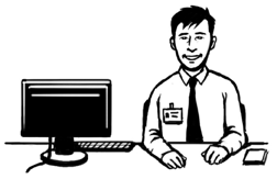 A man sitting at a desk with a computer on it. He is wearing a name badge and looking happy